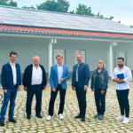 Projektverantwortliche stehen vor einem Gebäude des Parkfriedhofs in Olching, auf dem eine Photovoltaik-Anlage in Betrieb genommen wurde.