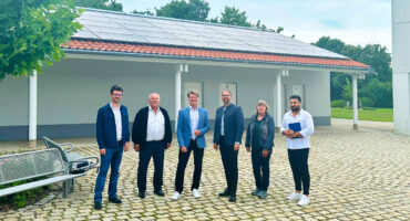 Projektverantwortliche stehen vor einem Gebäude des Parkfriedhofs in Olching, auf dem eine Photovoltaik-Anlage in Betrieb genommen wurde.