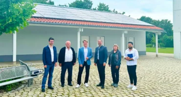 Projektverantwortliche der Stadt Olching und der Stadtwerke Olching stehen vor einem Gebäude des Parkfriedhofs in Olching auf dem eine PV-Anlage installiert wurde.