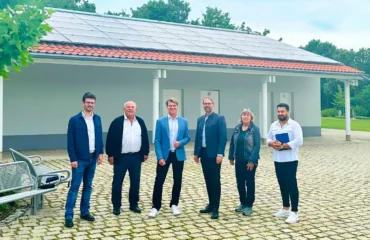 Projektverantwortliche der Stadt Olching und der Stadtwerke Olching stehen vor einem Gebäude des Parkfriedhofs in Olching auf dem eine PV-Anlage installiert wurde.
