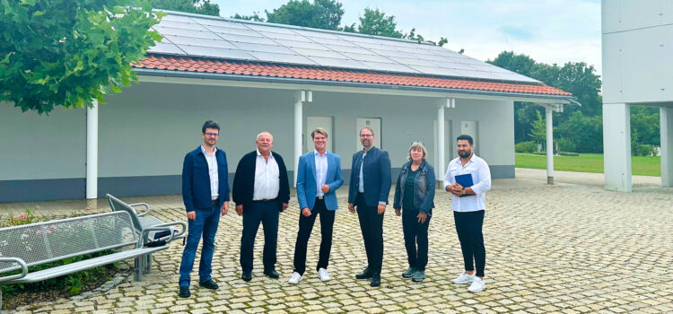 Projektverantwortliche stehen vor einem Gebäude des Parkfriedhofs in Olching, auf dem eine Photovoltaik-Anlage in Betrieb genommen wurde.