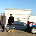 Der Geschäftsführer Thomas Grulke, der Erste Bürgermeister von Olching Herr Andreas Magg und der Projektleiter der Stadtwerke Olching Herr Firas Alzaghir stehen auf der Baustelle der geplanten PV-Freiflächenanlage vor einer aufgestellten Trafostation neben einem Fahrzeug der Stadtwerke Olching