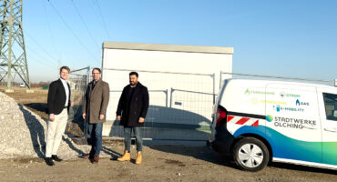 Der Geschäftsführer Thomas Grulke, der Erste Bürgermeister von Olching Herr Andreas Magg und der Projektleiter der Stadtwerke Olching Herr Firas Alzaghir stehen auf der Baustelle der geplanten PV-Freiflächenanlage vor einer aufgestellten Trafostation neben einem Fahrzeug der Stadtwerke Olching