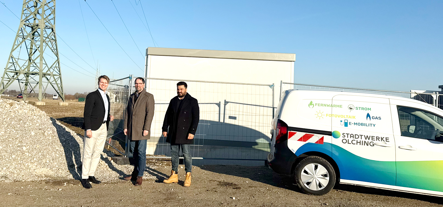 Der Geschäftsführer Thomas Grulke, der Erste Bürgermeister von Olching Herr Andreas Magg und der Projektleiter der Stadtwerke Olching Herr Firas Alzaghir stehen auf der Baustelle der geplanten PV-Freiflächenanlage vor einer aufgestellten Trafostation neben einem Fahrzeug der Stadtwerke Olching