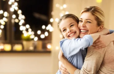 Imagebild Strom Lächelnde Frau und Mädchen umarmen sich. Im Hintergrund sind Lichterketten zu sehen.
